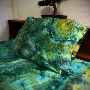 May include: A rectangular pillowcase and matching bed sheet featuring a vibrant tie-dye pattern in shades of emerald green, forest green, teal, and golden yellow. The fabric displays swirling, marbled color transitions with organic shapes.