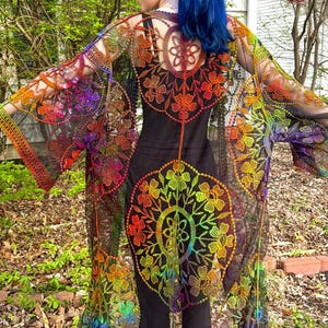May include: A sheer, rainbow-colored kimono-style garment with intricate floral embroidery. The garment features a black base with vibrant hues of red, orange, yellow, green, blue, and purple. The sleeves and back are adorned with large, circular floral patterns.