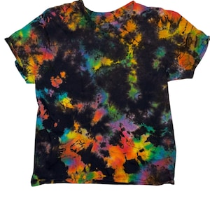 Op de afbeelding: Een zwart tie-dye T-shirt met een V-hals. Het shirt heeft een levendig patroon van regenboogkleuren, waaronder oranje, geel, groen, blauw en paars, tegen een zwarte achtergrond. Het shirt met korte mouwen is gemaakt van zacht materiaal.