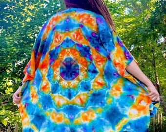 Puede incluir: Un vibrante kimono teñido anudado en tonos azules, naranjas y morados. La prenda de frente abierto presenta un patrón circular y mangas cortas. El diseño colorido y fluido es perfecto para un estilo bohemio o festivalero.