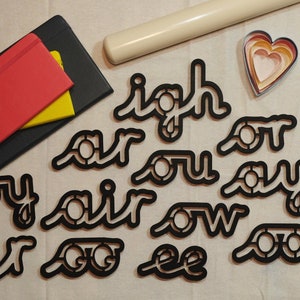 May include: A set of black cookie cutters shaped like the words "Igh", "Air", "Or", "You", "Say", "It", "Go", "Ee", and "Ow".