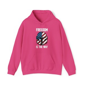 May include: A bright pink hooded sweatshirt with a front pocket and drawstring. The front features a graphic of a helmet with the American flag design and the text "FREEDOM IS THE WAY" in white.