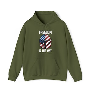 May include: Olive green hoodie with a front graphic featuring a helmet design incorporating the American flag and the text "FREEDOM IS THE WAY" in white. The hoodie has a drawstring hood and a front pocket.