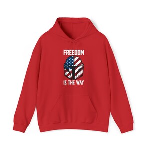 May include: A red hooded sweatshirt with a front pocket and drawstring. The graphic on the front features a helmet design with the American flag and the text "FREEDOM IS THE WAY" in white.