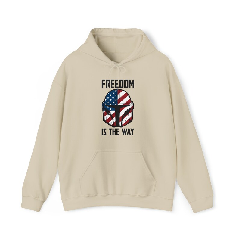 May include: A beige hoodie with a front graphic featuring a helmet design incorporating the American flag. The text "FREEDOM IS THE WAY" is printed above and below the helmet. The hoodie has a front pocket and a drawstring hood.