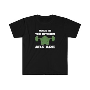 Peut inclure: T-shirt noir avec du texte blanc qui dit "Made in the Kitchen Abs Are" et un personnage de dessin animé vert soulevant une barre.