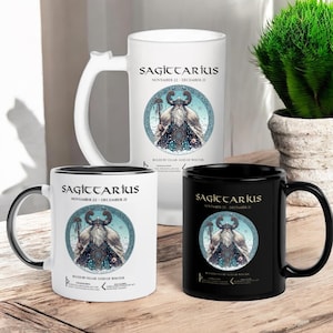 May include: Three ceramic mugs with black rims. The mugs feature a white background with a black and blue illustration of a bearded man in a horned helmet. The text "SAGITTARIUS" is printed in black on the mugs. The text "NOVEMBER 22 - DECEMBER 21" is printed in black below the illustration. The text "RULED BY ULLAR GOD OF WINTER" is printed in black below the date.