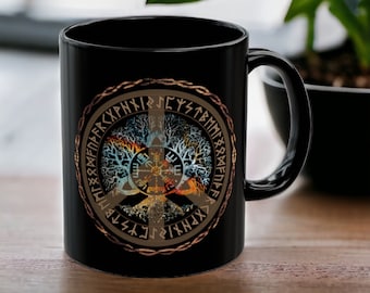 May include: Black ceramic mug with a gold and brown design featuring a tree of life with a compass in the center and runes around the outside. The runes are in a circle around the tree of life.