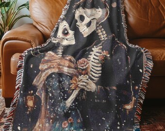 May include: Woven throw blanket featuring a romantic skeleton couple. The design depicts two skeletons embracing, holding flowers, against a dark background with a starry effect. The blanket has a fringed edge with red, white, and blue accents.