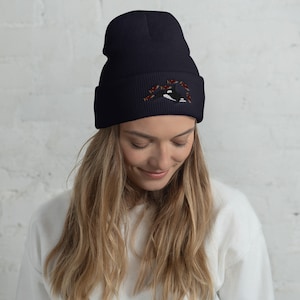 May include: A navy blue beanie with a black and white orca whale design and red fish embroidered on the front.
