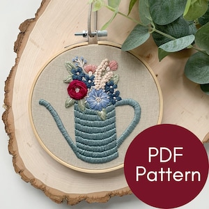 Op de afbeelding: Borduurwerk in een hoepel met een blauwe gieter gevuld met kleurrijke bloemen. De hoepel is van hout en heeft een beige stoffen achtergrond. De tekst "PDF Pattern" is zichtbaar in de rechterbenedenhoek van de afbeelding.