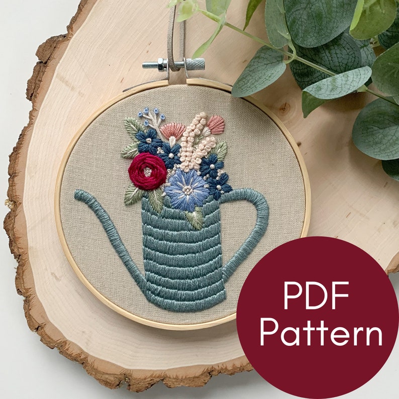 Op de afbeelding: Borduurwerk in een hoepel met een blauwe gieter gevuld met kleurrijke bloemen. De hoepel is van hout en heeft een beige stoffen achtergrond. De tekst "PDF Pattern" is zichtbaar in de rechterbenedenhoek van de afbeelding.
