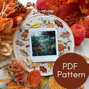 Może przedstawiać: Biały tamborek do haftu z wzorem jesiennych liści, dyni i zdjęciem. Tamborek jest otoczony jesiennymi liśćmi i kwiatami. Tekst "PDF Pattern" znajduje się na brązowym tle.