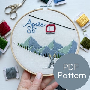 Peut inclure: Un gros plan d'un cerceau de broderie terminé avec une scène d'hiver. La broderie représente un téléphérique, des montagnes et des skis. Le texte "Après Ski" est brodé en fil bleu. Le cerceau est tenu par une main. Le texte "Modèle PDF" est sur un cercle gris dans le coin inférieur droit.