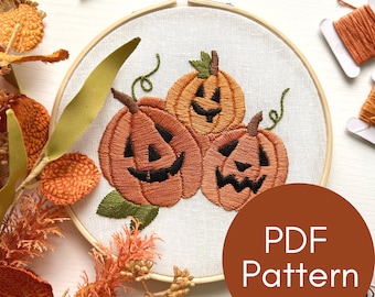 May include: Embroidered Halloween pumpkin design in an embroidery hoop. The design features three orange pumpkins with black eyes, noses, and mouths. The pumpkins are surrounded by green leaves. The text "PDF Pattern" is visible in the lower right corner of the image.