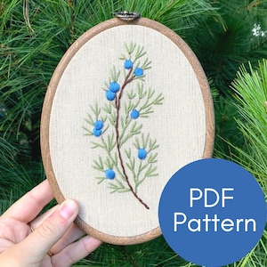 Può includere: Arte di ricamo in cerchio con un rametto di ginepro con bacche blu. Il cerchio è in legno e ha un tessuto di lino naturale. Il testo "PDF Pattern" è visibile nell'angolo in basso a destra dell'immagine.