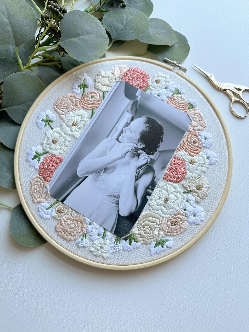 May include: A black and white photo of a person is framed with a hoop of embroidered fabric. The fabric is white with pink and white flowers.