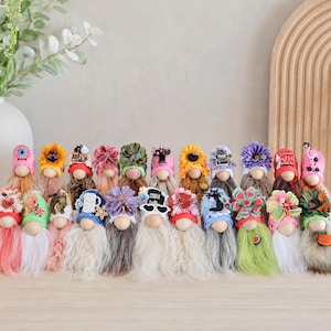 May include: A collection of decorative gnomes with wooden heads, long white beards, and colorful hats adorned with flowers and other embellishments. The gnomes have various hat designs, including floral patterns and text.