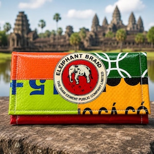 May include: A rectangular wallet made of recycled material featuring a vibrant patchwork of orange, lime green, yellow, and red. A circular logo in the center displays an elephant illustration with the text Elephant Brand The Siam Cement Public Company Limited.