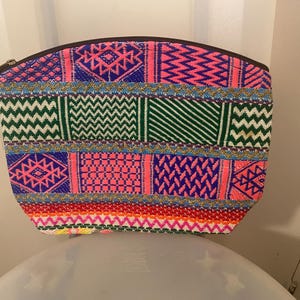 Könnte beinhalten: Eine bunte gewebte Stofftasche mit Reißverschluss. Die Tasche hat ein geometrisches Muster in den Farben Pink, Grün, Blau und Gelb.
