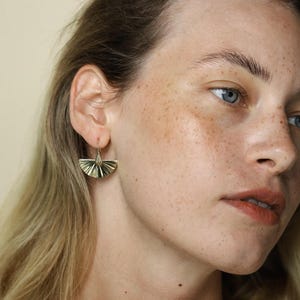 Peut inclure: Une paire de boucles d'oreilles en forme d'éventail dorées avec un design géométrique délicat. Les boucles d'oreilles pendent du lobe de l'oreille et ont un style simple et élégant.