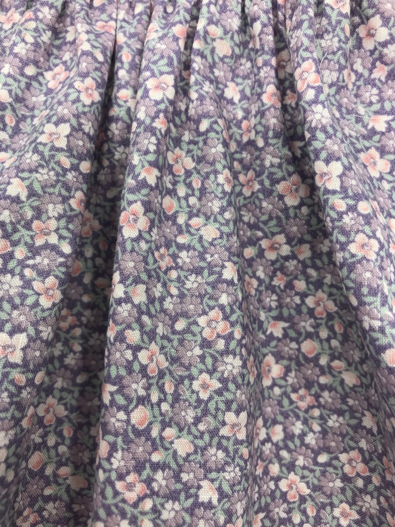 May include: Close-up of a purple fabric with a small white and pink floral pattern.