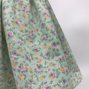May include: A green skirt with a floral print featuring small purple and orange flowers. The skirt is made of a soft, lightweight fabric.