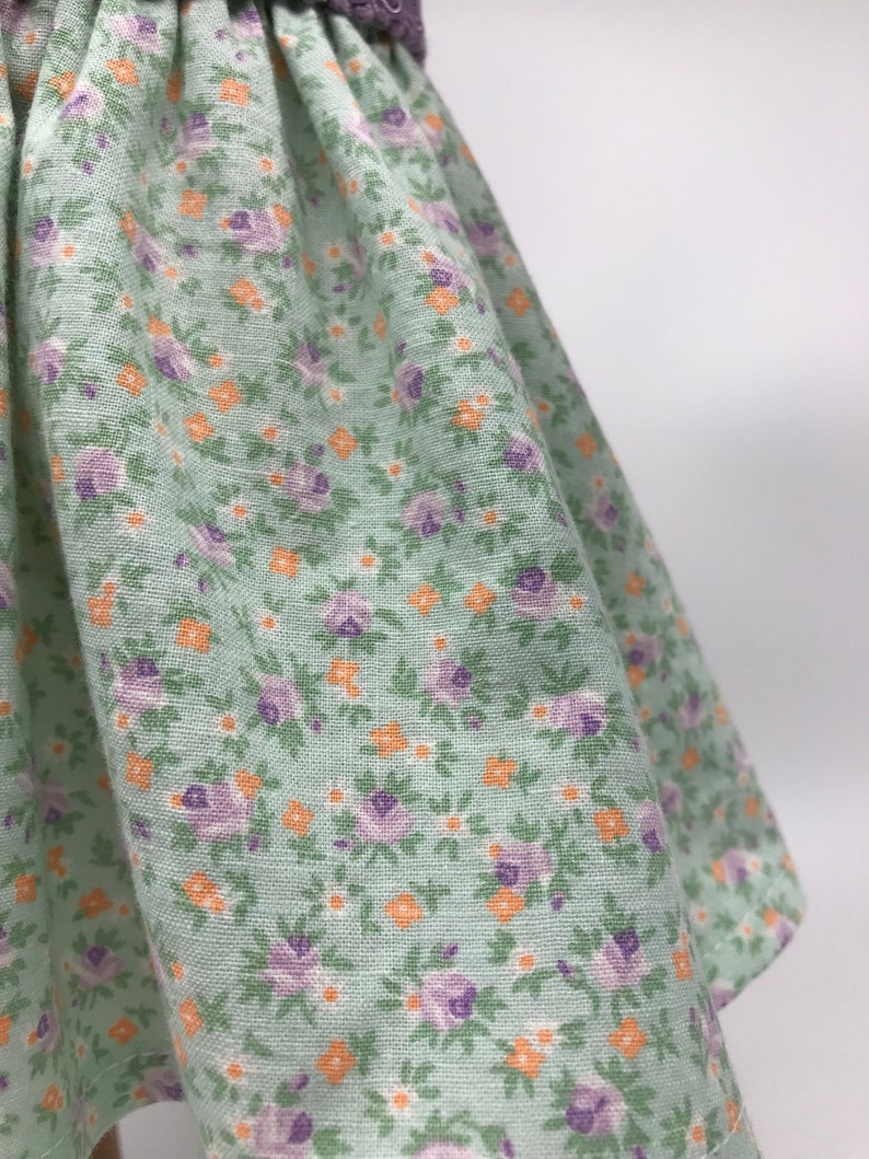 May include: A green skirt with a floral print featuring small purple and orange flowers. The skirt is made of a soft, lightweight fabric.