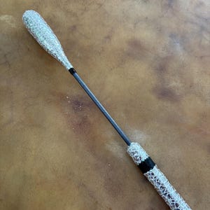 May include: A drum beater with a silver and white patterned head and handle. The handle is a dark gray color with a black band near the base. The drumstick is designed for percussion instruments.