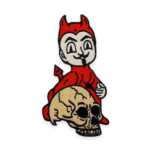Może przedstawiać: Haftowana naszywka przedstawiająca kreskówkowego diabła w kolorze czerwonym, z rogami i ogonem, siedzącego na beżowej czaszce. Diabeł ma białą twarz z psotnym wyrazem twarzy i czarną bródką. Naszywka ma czarną obwódkę.