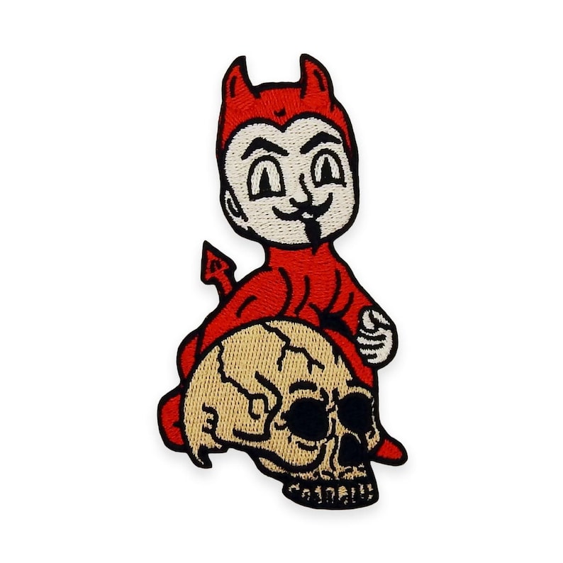 May include: Embroidered patch depicting a cartoon devil in red, with horns and a tail, perched on a tan skull. The devil has a white face with a playful expression and a black goatee. The patch has a black border.