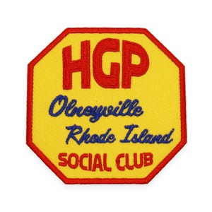 May include: A yellow octagon-shaped patch with red stitching around the edges. The patch has the text "HGP" in red, "Olneyville Rhode Island" in blue, and "SOCIAL CLUB" in yellow.