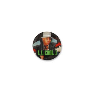 Puede incluir: Un botón redondo con un retrato de LL Cool J con un sombrero fedora y una chaqueta negra con detalles azules y rojos. El texto "L.L. COOL J" se muestra en verde en la parte inferior del botón.