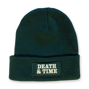 May include: A dark green beanie with a black patch that says "DEATH & TIME" in white letters.