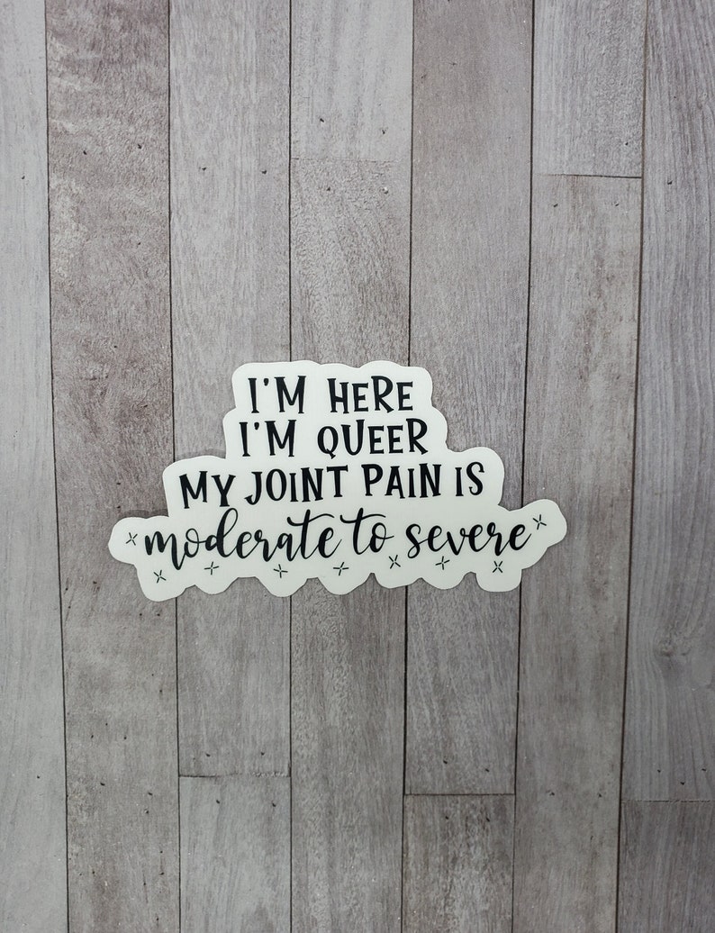 May include: White sticker with black text that reads "I'm here, I'm queer, my joint pain is *moderate to severe*" with stars around the text.