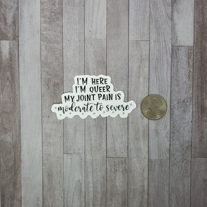 May include: White sticker with black text that reads "I'm here I'm queer My joint pain is moderate to severe".