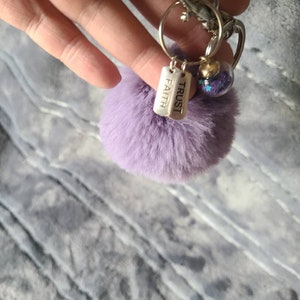 May include: Purple fluffy keychain with a silver charm that says "TRUST" and "FAITH" and a clear glass charm with glitter inside.