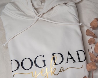 May include: A cream-colored hoodie with the text "DOG DAD" in black lettering and "yes, ka" in gold lettering.