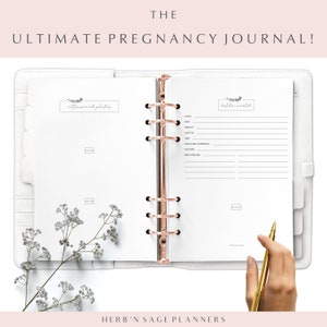 May include: A white pregnancy journal with a rose gold binder. The cover has the text "THE ULTIMATE PREGNANCY JOURNAL!" and the words "ultrasound photos" and "hello world" are written on the pages.
