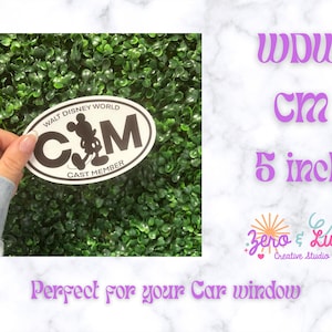 May include: An oval-shaped white sticker with a black border and black text that reads WALT DISNEY WORLD CAST MEMBER. The centre features a black silhouette of Mickey Mouse replacing the letter A in the letters CM. The sticker is 12.7 cm wide.