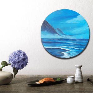 Könnte beinhalten: Ein rundes Gemälde, das eine Meereslandschaft mit einer Bergkette im Hintergrund zeigt. Der Himmel ist hellblau mit ein paar Wolken. Das Wasser ist tiefblau mit weißen Wellen. Das Gemälde ist in einem dunklen Holzrahmen gerahmt.