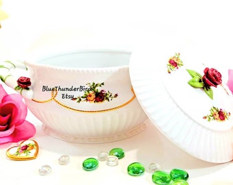 May include: White porcelain soup tureen with a lid, featuring a floral pattern with red, yellow, and green roses. The tureen has a gold trim and a fluted design. The lid has a 3D rose on top.