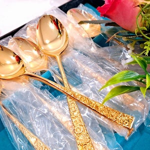 May include: Set of gold-plated spoons with ornate designs, packaged in a blue box with clear plastic wrapping. The spoons are arranged in a fan shape, with the handles facing outward.