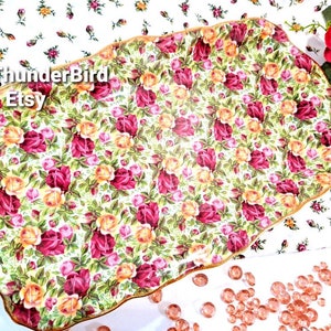 May include: A white ceramic serving tray with a scalloped edge and a gold trim. The tray is decorated with a floral pattern of red, yellow, and pink roses.