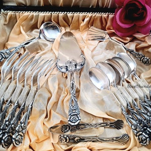 May include: A set of silver-plated cutlery with rose-shaped handles, including forks, spoons, a cake server, and sugar tongs, displayed in a velvet-lined box.