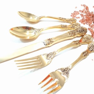May include: A set of gold-plated silverware with ornate designs. The set includes a knife, fork, and two spoons.