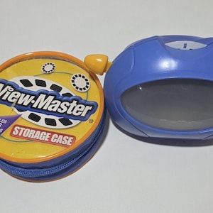 May include: A round yellow and blue View-Master storage case with a zipper, labeled to hold 48 reels, positioned next to a blue plastic View-Master viewer with a yellow lever and a gray viewing lens on the front of the device.