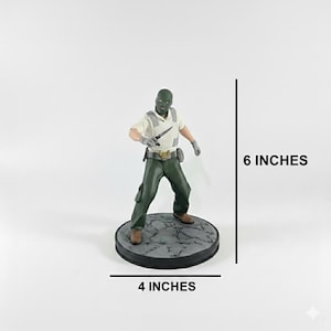 May include: A figurine of a character in a green mask, shirt, and pants, holding a knife. The figure stands on a 4-inch diameter base and is 6 inches tall. The base is a dark gray color with a textured surface.