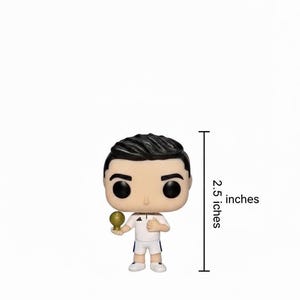 May include: A Funko Pop vinyl figure of a footballer, 6.35 cm tall, in a white uniform. The figure has black hair and large black eyes, and is holding a golden trophy.