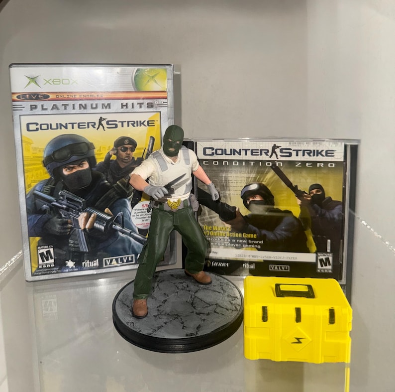 May include: An assortment of Counter-Strike themed items. Includes an Xbox game case, a PC game case, a figurine of a character holding knives, and a yellow box with a lightning bolt symbol.